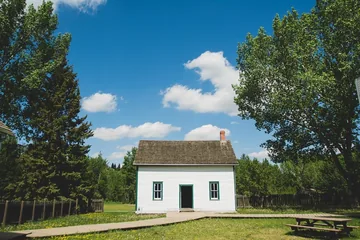 Photo of a small white house under trees and a blue sky